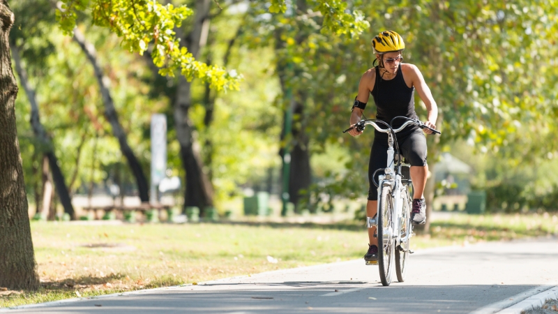 Person riding an e-bike on a sunny park trail surrounded by trees
