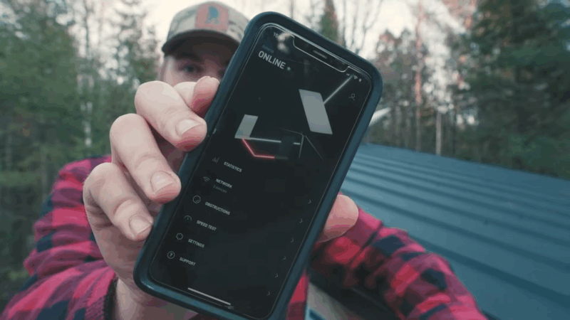 A person shows the Starlink Roam app on a smartphone with an active online connection in a forested outdoor location