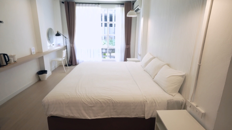 A bright, minimalist hotel room with a large bed and work desk offers an affordable accommodation option for travelers