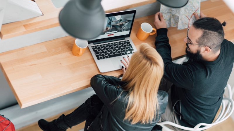 Two travelers look at accommodation options on a laptop while planning how to find hidden value for their trip