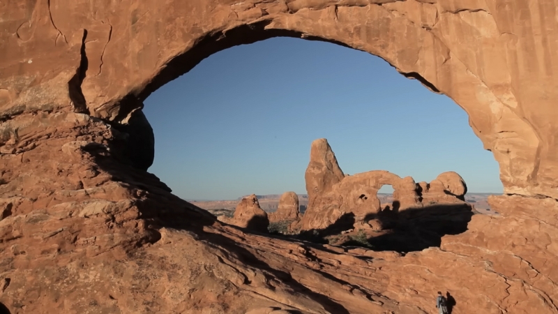 A giant rock arch frames more sandstone formations under a clear sky in Arches National Park