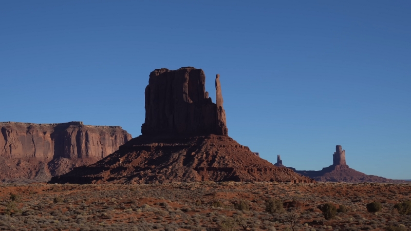 A massive red sandstone butte rises above the flat desert floor in Monument Valley