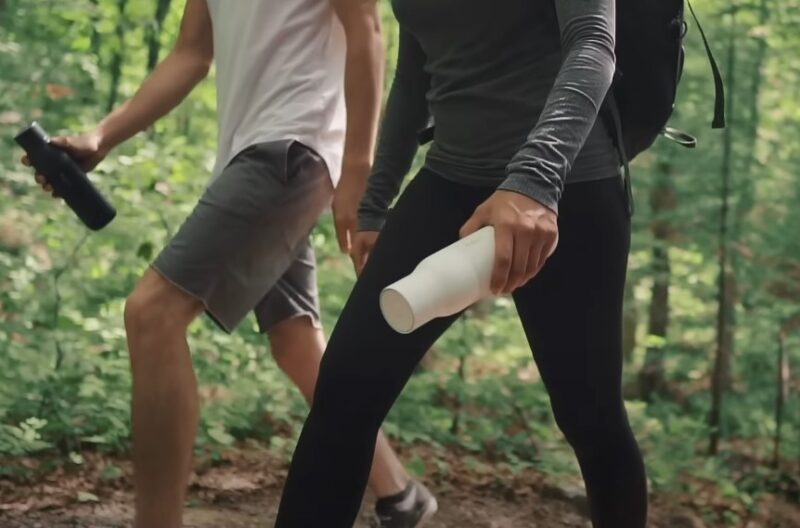 Two hikers walking through the woods, holding water bottles