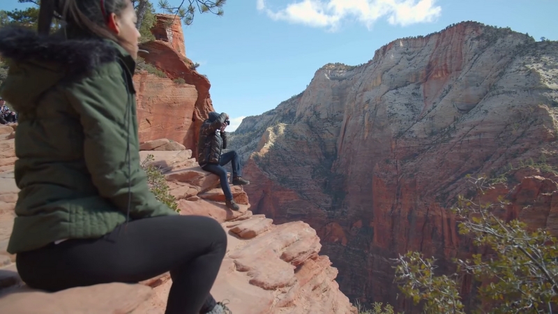Hikers sit on a rocky ledge in Zion National Park, overlooking steep red canyon walls
