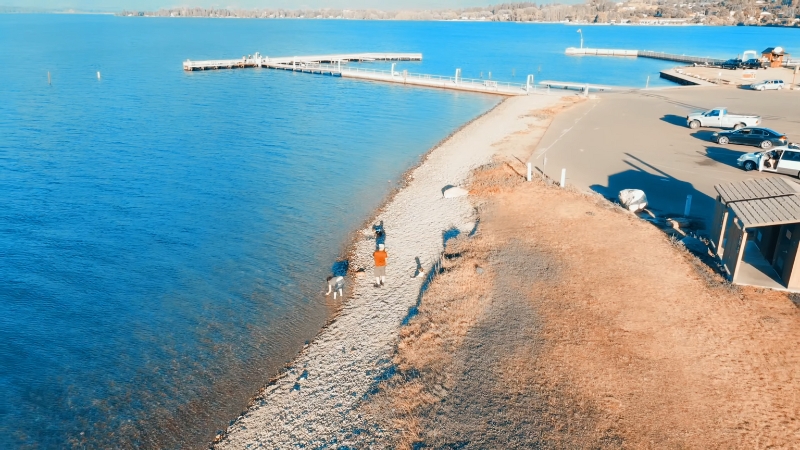 People walk along the small rocky beach at Salish Point with docks and clear blue water in the background