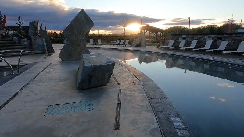 Bozeman Hot Springs outdoor pool at sunset with stone sculptures and empty lounge chairs