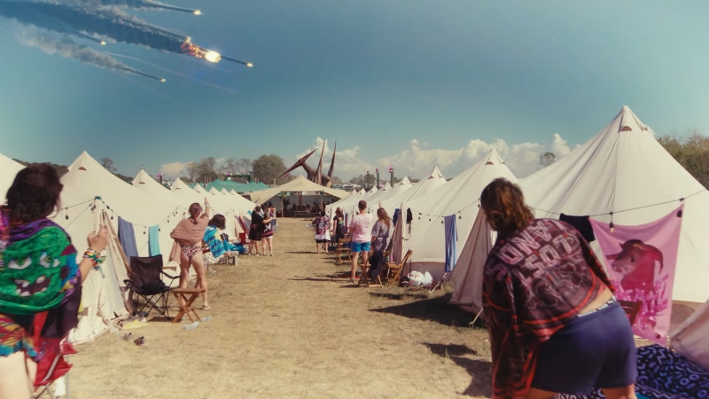 Festival campers walk between rows of white tents under a clear sky at Lost Lands festival 2025
