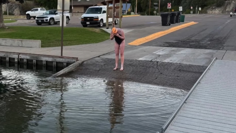 A person stands at the boat ramp edge of Flathead Lake, preparing to enter the water for a swim