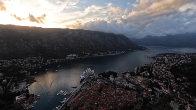 A view of Kotor Bay in Montenegro with mountains, coastal towns, and a cruise ship at sunset