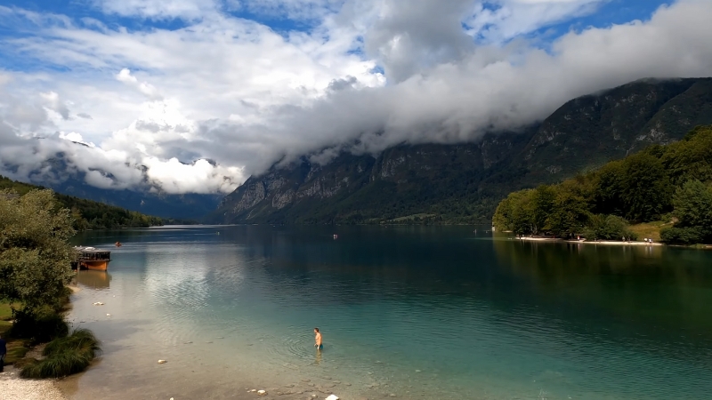 Clear waters of Lake Bohinj surrounded by forests and mountains under a cloudy summer sky in Slovenia