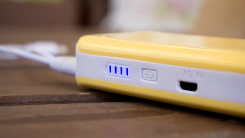 A yellow portable phone charger with blue indicator lights plugged in and charging