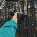 A hiker in a teal jacket holds a camera in the forest, symbolizing smart side hustles for hikers who love taking photos