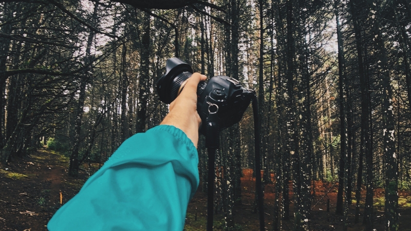 A hiker in a teal jacket holds a camera in the forest, symbolizing smart side hustles for hikers who love taking photos