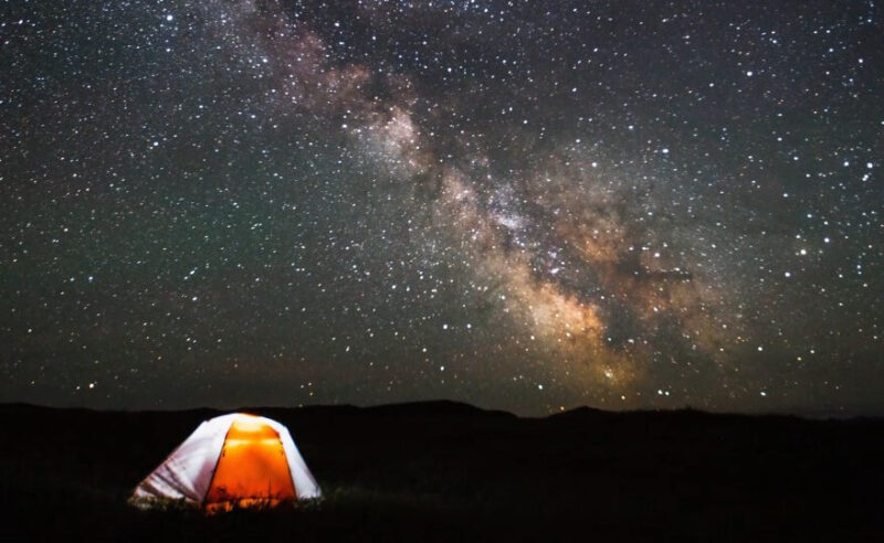 A brightly lit tent under a starry night sky