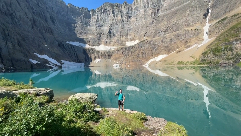 A hiker stands at the edge of Iceberg Lake in Montana, surrounded by turquoise water and towering cliffs