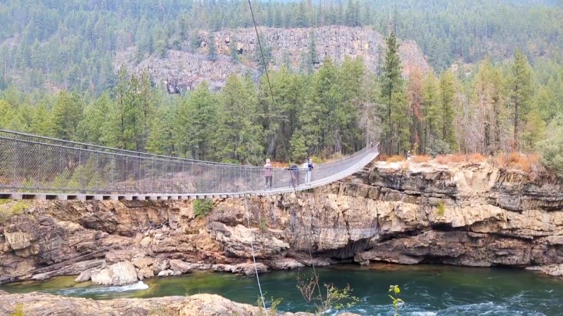 Two people cross the swinging bridge over the Kootenai River in Montana