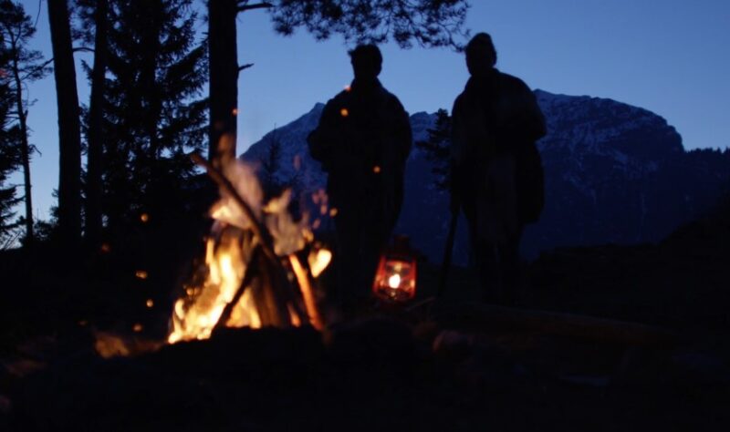 Two persons standing next to a fire during night camping