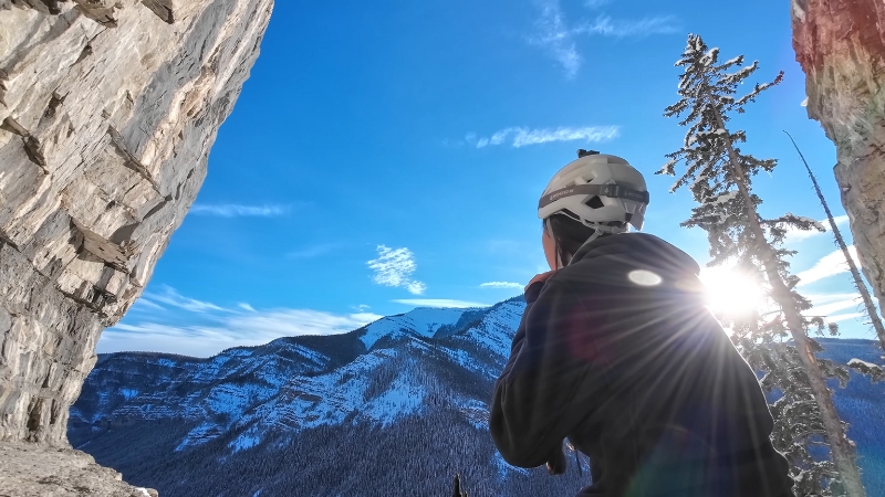 Hiker wearing a helmet looks out at snowy mountain peaks and forests framed by rock walls in Montana