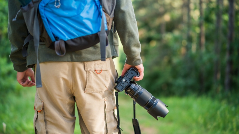 A hiker with a backpack holds a camera on a forest trail, showing the idea of selling presets and LUTs for hiking photography