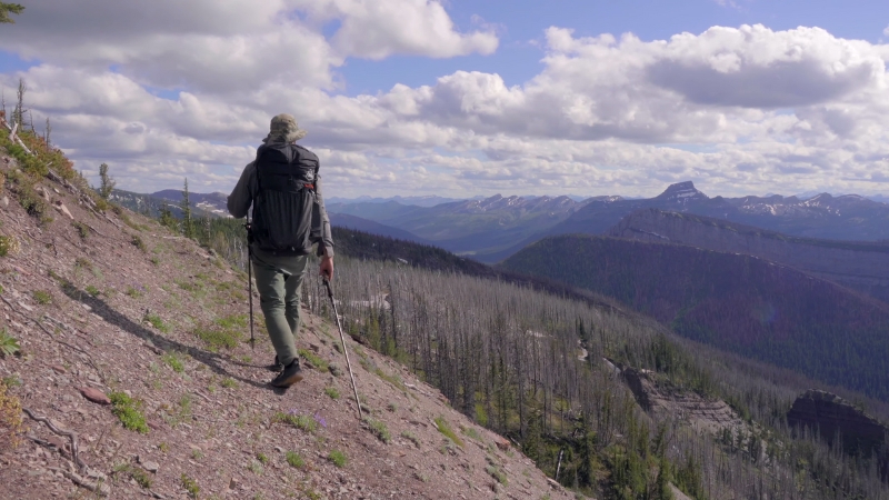 A hiker walks along a steep slope in Montana’s Bob Marshall Wilderness with wide views of mountains and valleys