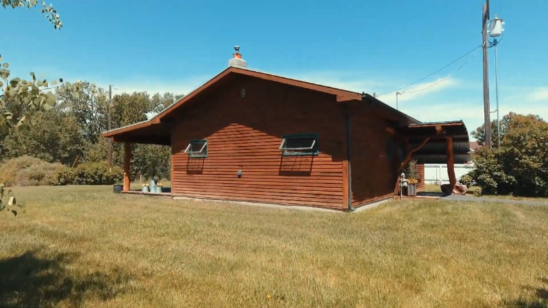 A wooden cabin on an open grassy lot under a clear blue sky, showing the Gallatin River Guest Cabin near Big Sky