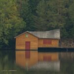 A secluded wooden cabin on a calm lake surrounded by dense forest, representing hidden cabins near Big Sky Montana