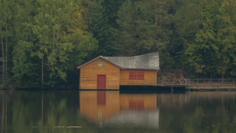 A secluded wooden cabin on a calm lake surrounded by dense forest, representing hidden cabins near Big Sky Montana
