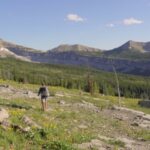 A hiker walks through an open alpine meadow in the Bob Marshall Wilderness