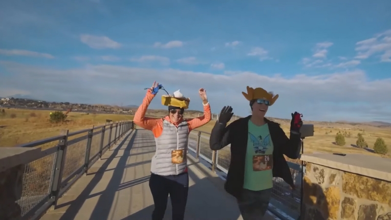 Two runners in festive hats raise their hands while crossing a bridge during Huffin’ For The Stuffin’