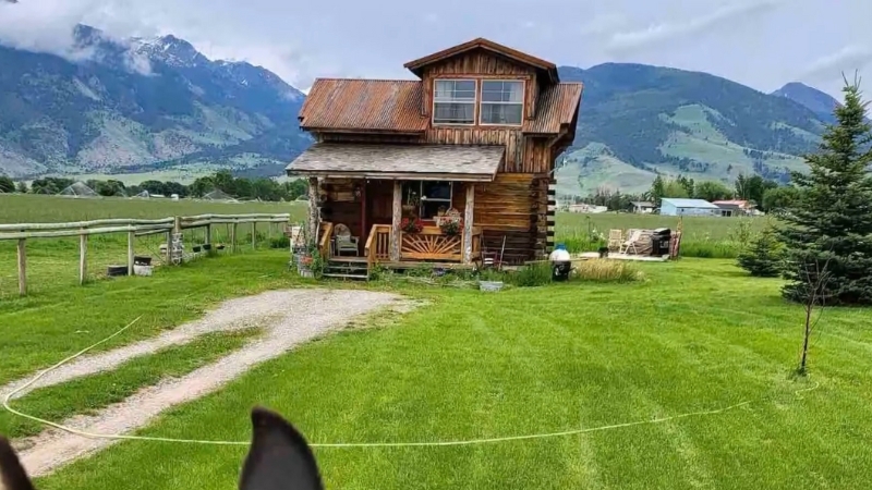 A small wooden cabin on a green field with mountain views, showing the Lost Antler Cabin in Paradise Valley