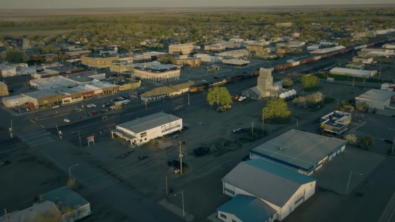 A quiet aerial view of Glasgow, Montana with small businesses, homes, and a long freight train running through town