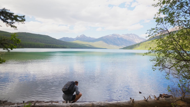 A couple enjoys a quiet moment by the clear water of Kintla Lake with mountain views in the distance