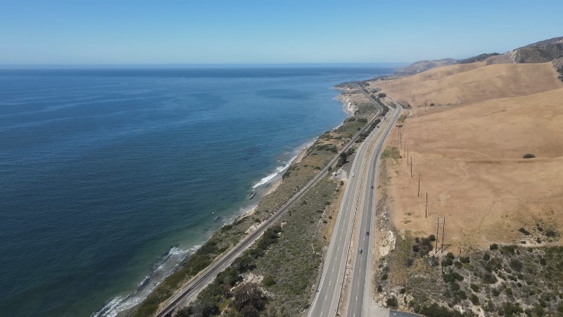 Aerial view of the Pacific Coast Highway in California running along the ocean with dry hills on one side