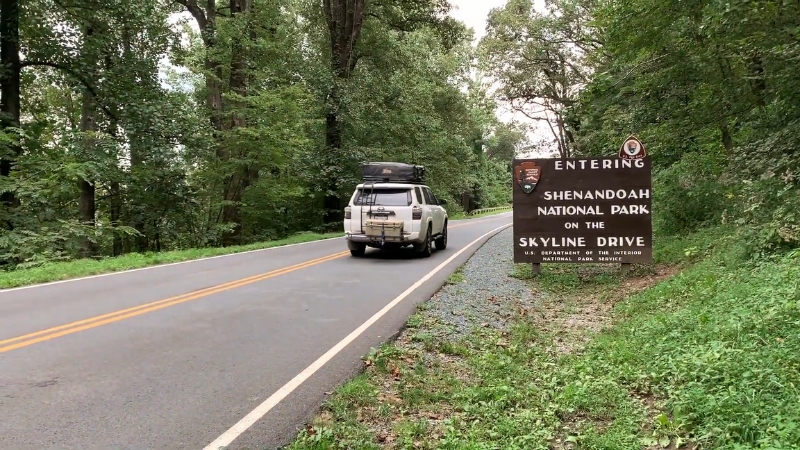A car enters Shenandoah National Park on Skyline Drive surrounded by green forest