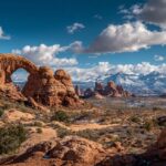 Natural rock arches and red sandstone formations with mountains in the distance