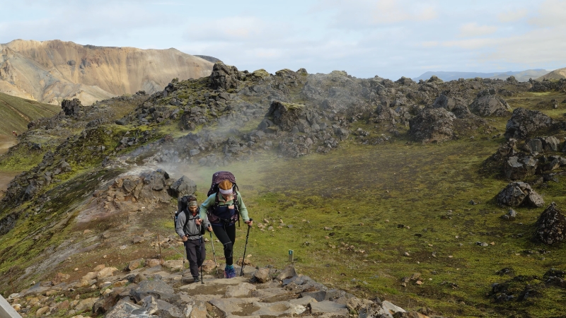 Hikers walk up a rocky trail in Landmannalaugar with mountains in the background