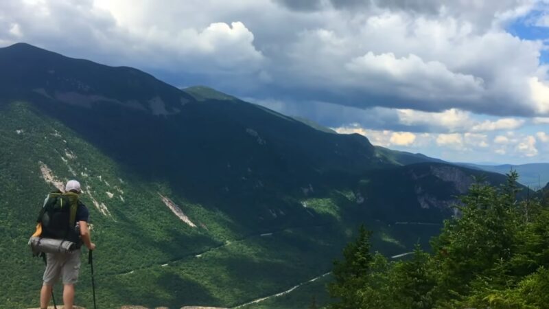 Hiker with a backpack overlooks a wide valley in the Appalachian mountains during a trail hike