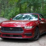 Red Ford Mustang convertible parked on a forest road