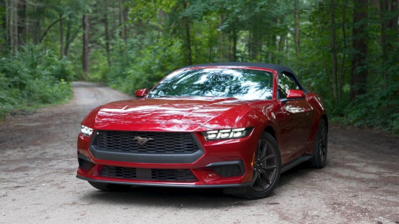 Red Ford Mustang convertible parked on a forest road