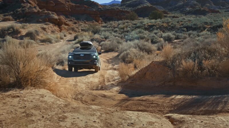 Subaru Outback driving on a rugged dirt road through a dry mountain landscape