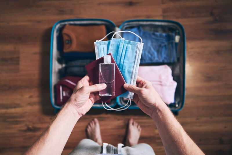 Traveler packing essentials like passport, face masks, and sanitizer for a safe trip