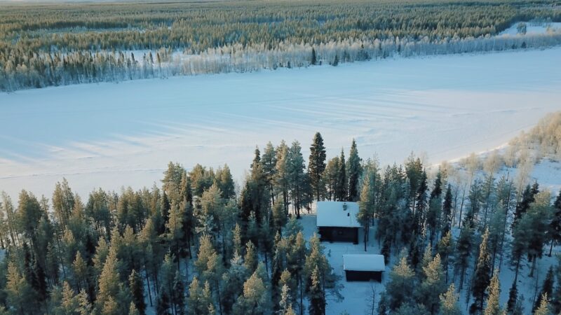 Snow-covered cabins sit among pine trees beside a frozen lake